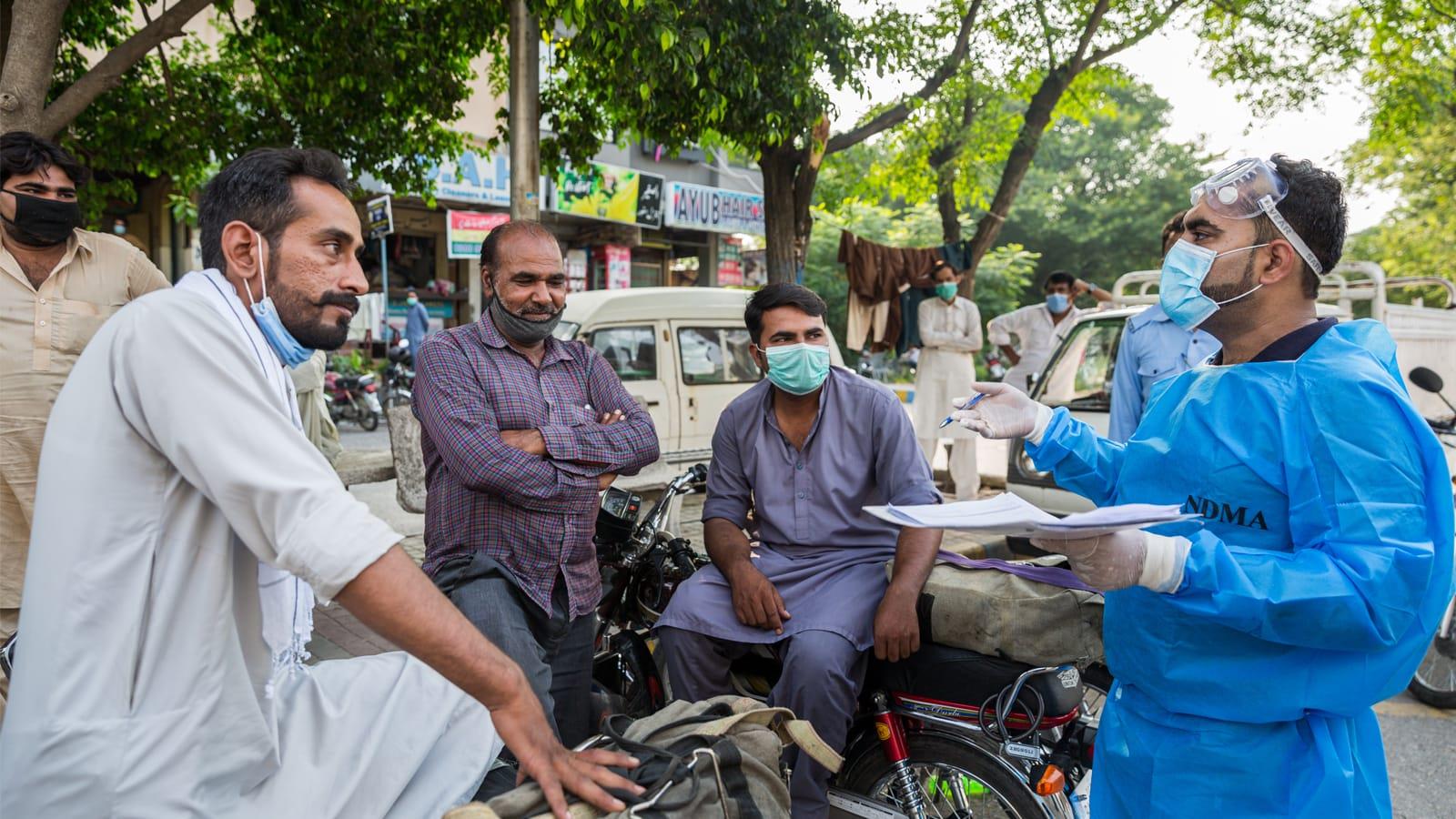 Photo of a doctor speaking with a small group of workers on a street in Pakistan.