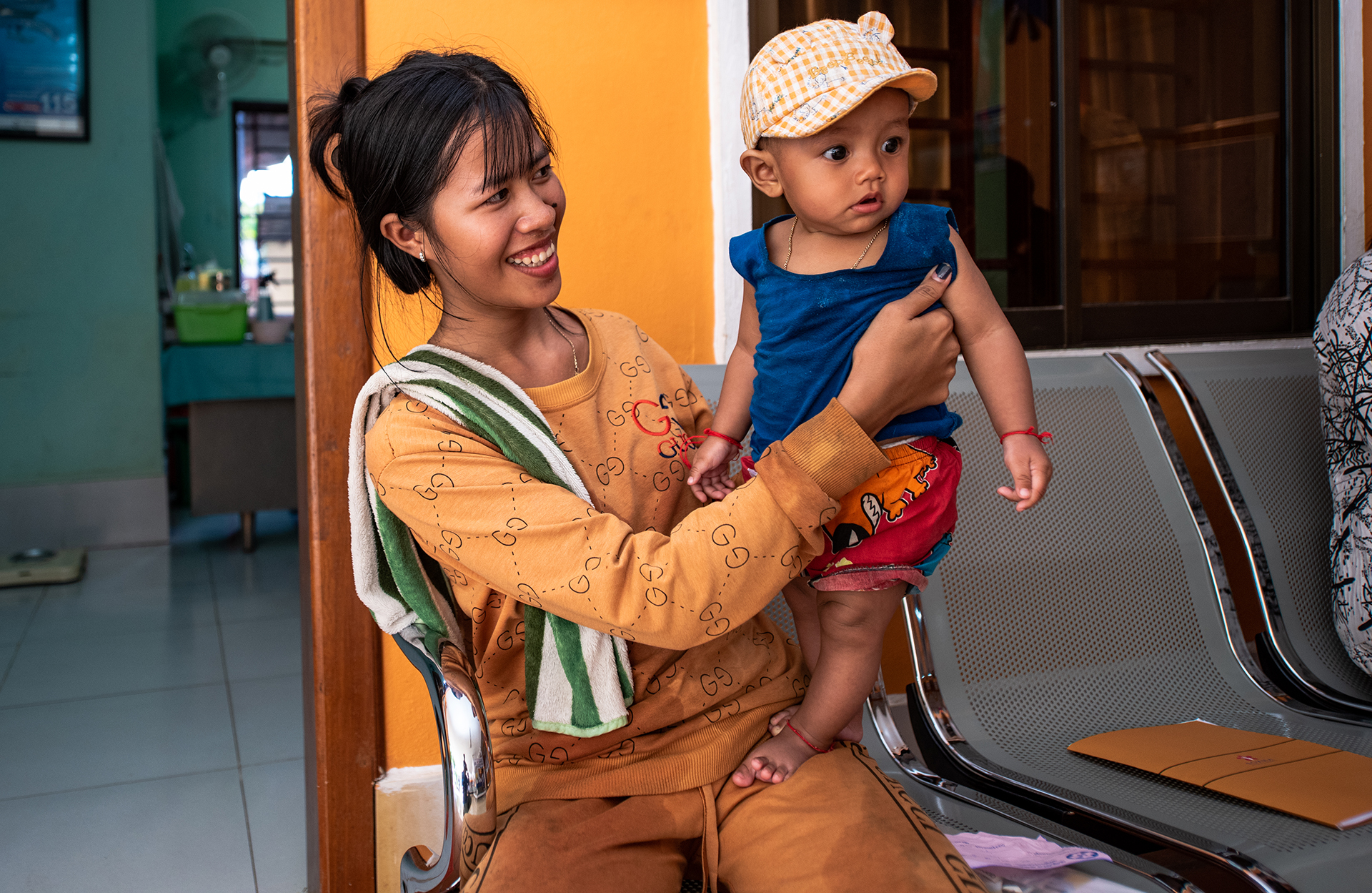 Mrs Say Sa smiles as she holds up her toddler on seats at a health clinic.