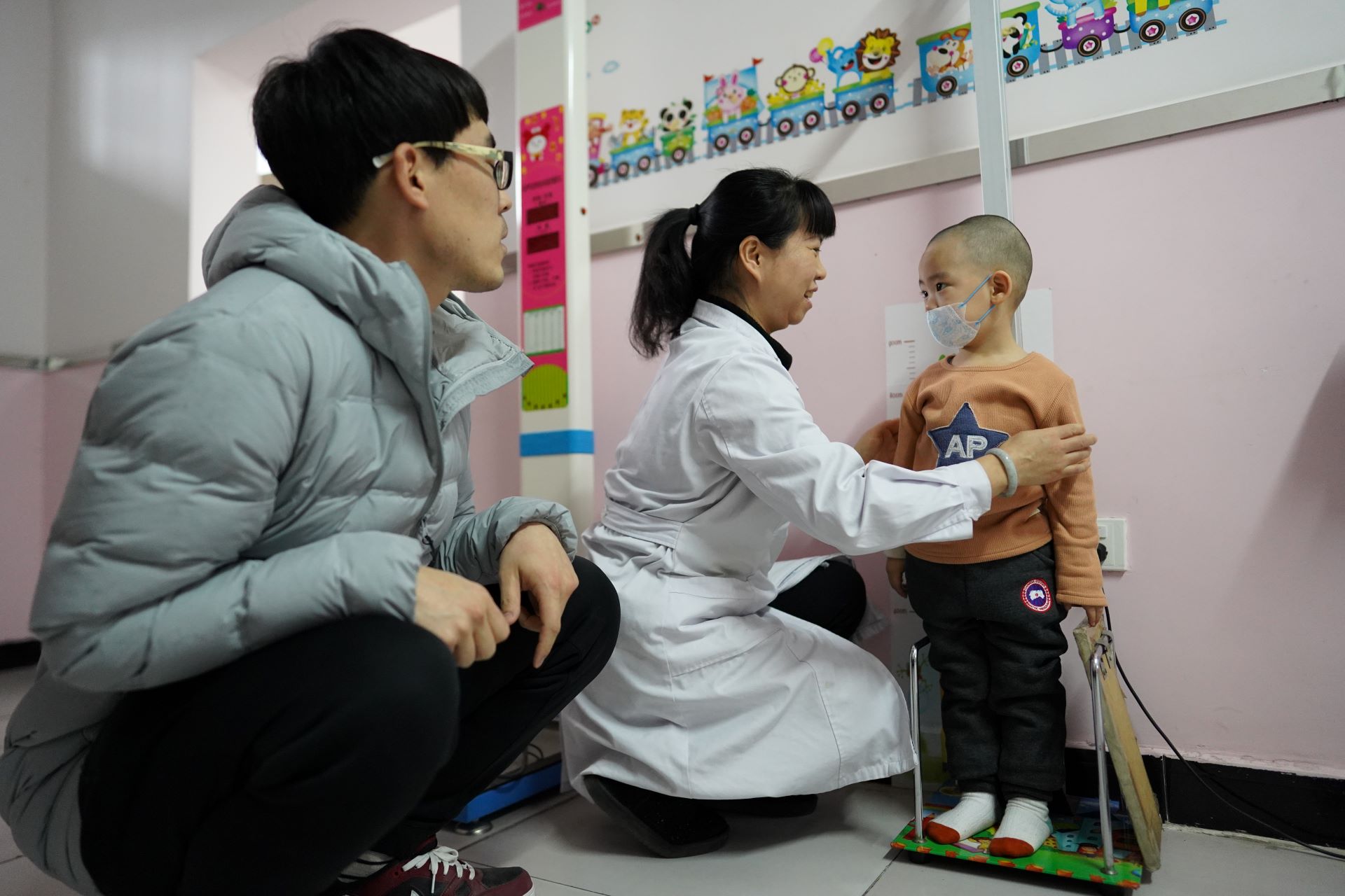 Father and child at a hospital for consultation. Child is being measured.