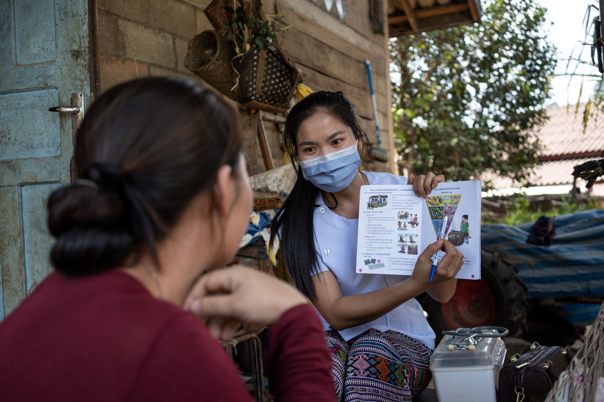 A health worker holds a pamphlet to explain nutrition to a young female.