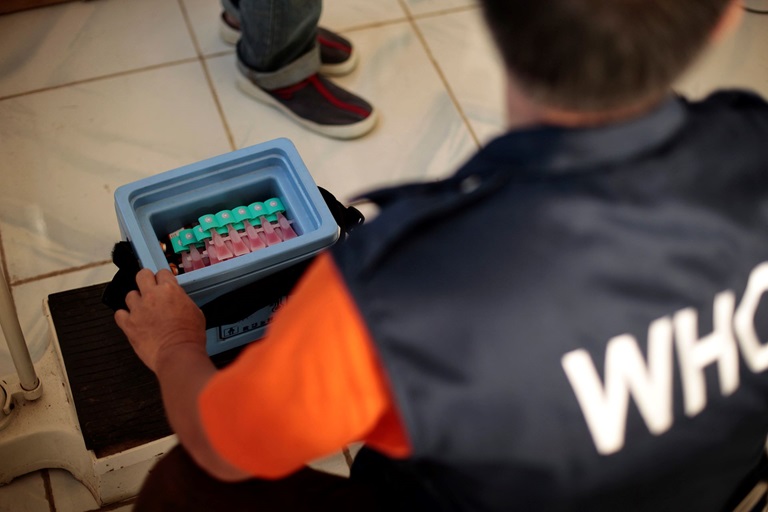 A WHO staff member looks down on an open old storage box full of vaccines.